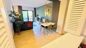 Een moderne woonkamer met een bank, eettafel, stoelen, een plant in pot en een groot raam.