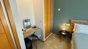 A compact bedroom with a wooden desk, a bedside table with a lamp, and a bed with a wooden headboard.