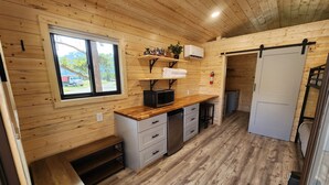 Una cocina compacta con paredes de madera, una ventana, un microondas y un lavamanos.