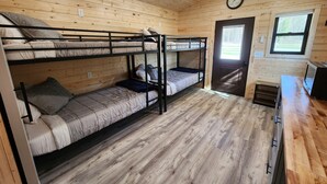 Un dormitorio con literas, dos camas dobles, piso de madera, una puerta, una ventana y un televisor.