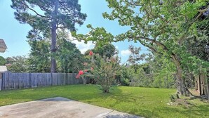 A backyard with a concrete patio, a wooden fence, and various trees and shrubs. - Coastal Comfort - 15 min to Beach, 10 min to City (Savannah)