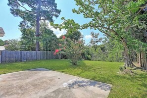 A backyard with a concrete patio, a wooden fence, and various trees and shrubs. - Coastal Comfort - 15 min to Beach, 10 min to City (Savannah)