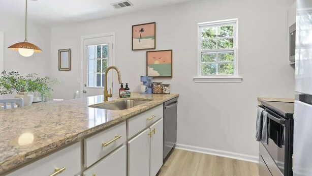 A kitchen with a granite countertop, stainless steel appliances, and a window with a view of greenery. - Coastal Comfort - 15 min to Beach, 10 min to City (Savannah)
