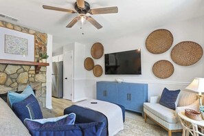 A living room with a stone fireplace, a ceiling fan, a flat-screen TV, and a blue cabinet. - Coastal Comfort - 15 min to Beach, 10 min to City (Savannah)