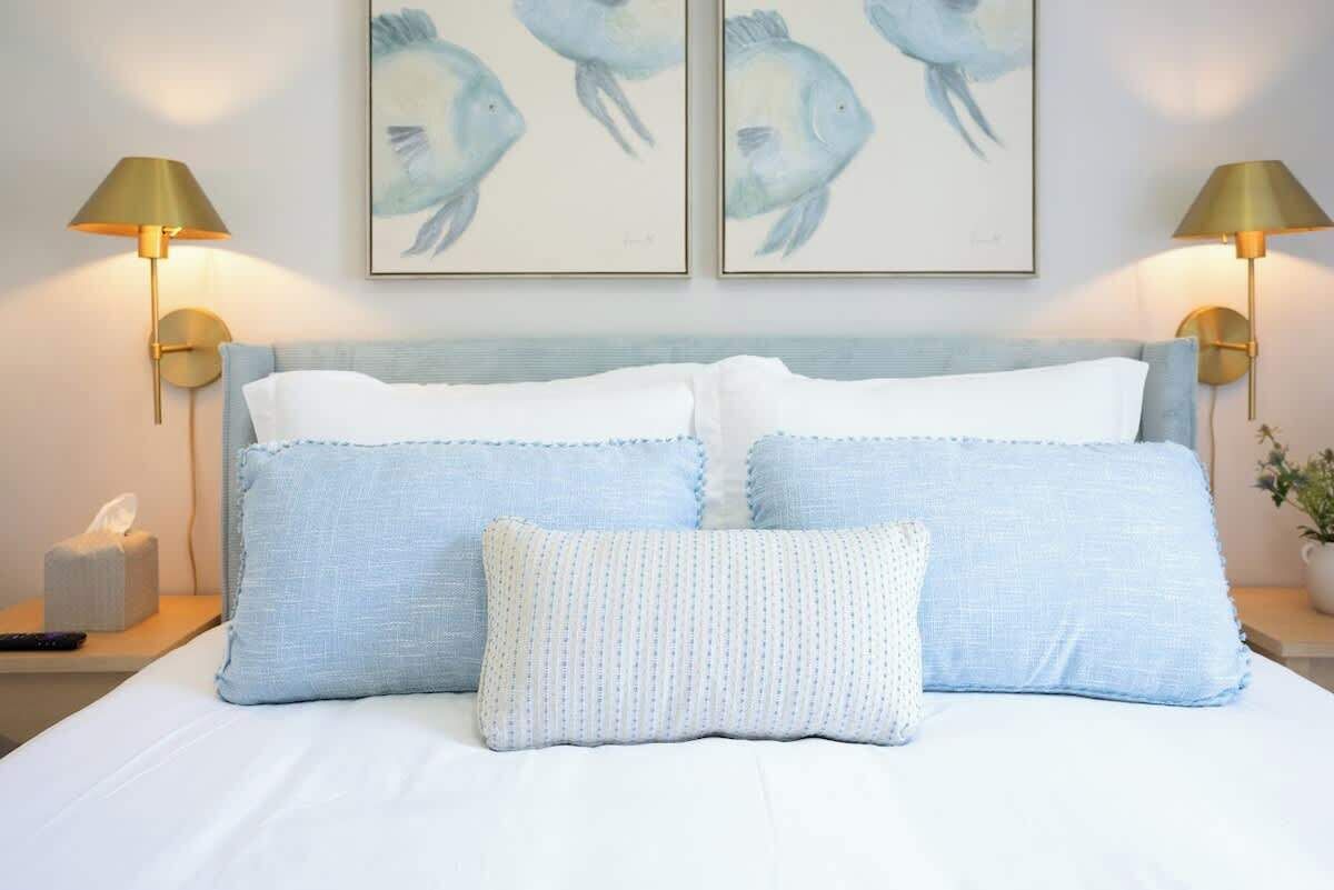 A neatly made bed with two pillows and a decorative pillow, flanked by two wall-mounted lamps.