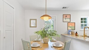 A dining area with a round table, chairs, a vase with greenery, and wall art. - Coastal Comfort - 15 min to Beach, 10 min to City (Savannah)