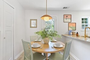 A dining area with a round table, chairs, a vase with greenery, and wall art. - Coastal Comfort - 15 min to Beach, 10 min to City (Savannah)