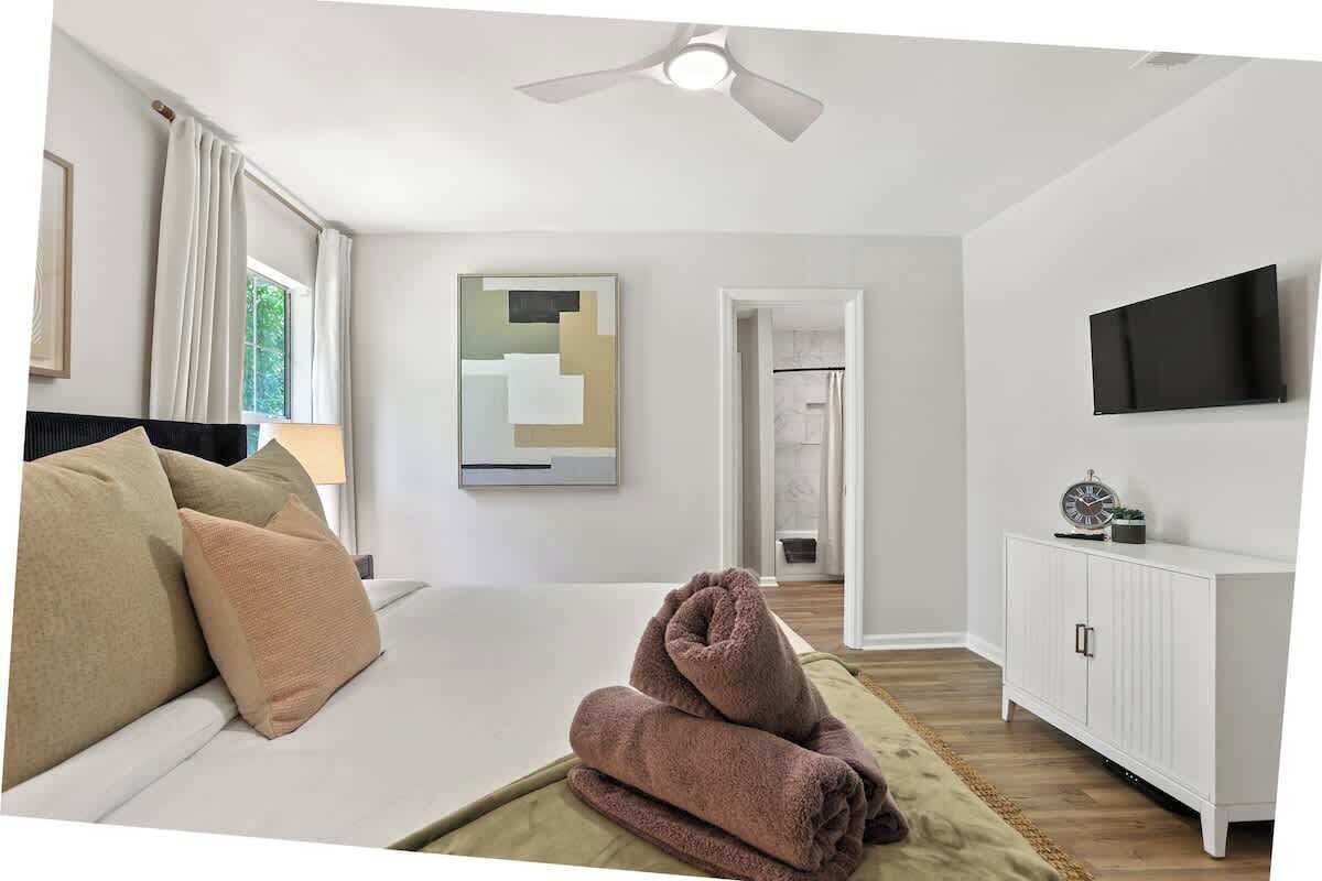 A hotel room with a bed, a TV, a painting, and a view of the outside.