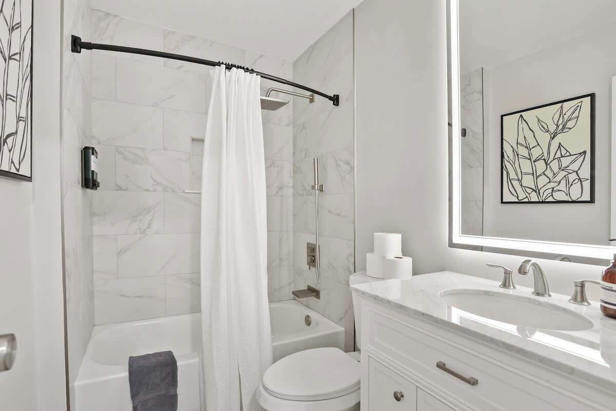 A modern bathroom with a bathtub, toilet, and a large mirror above the sink.
