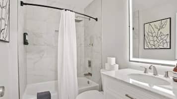 A modern bathroom with a bathtub, toilet, and a large mirror above the sink.