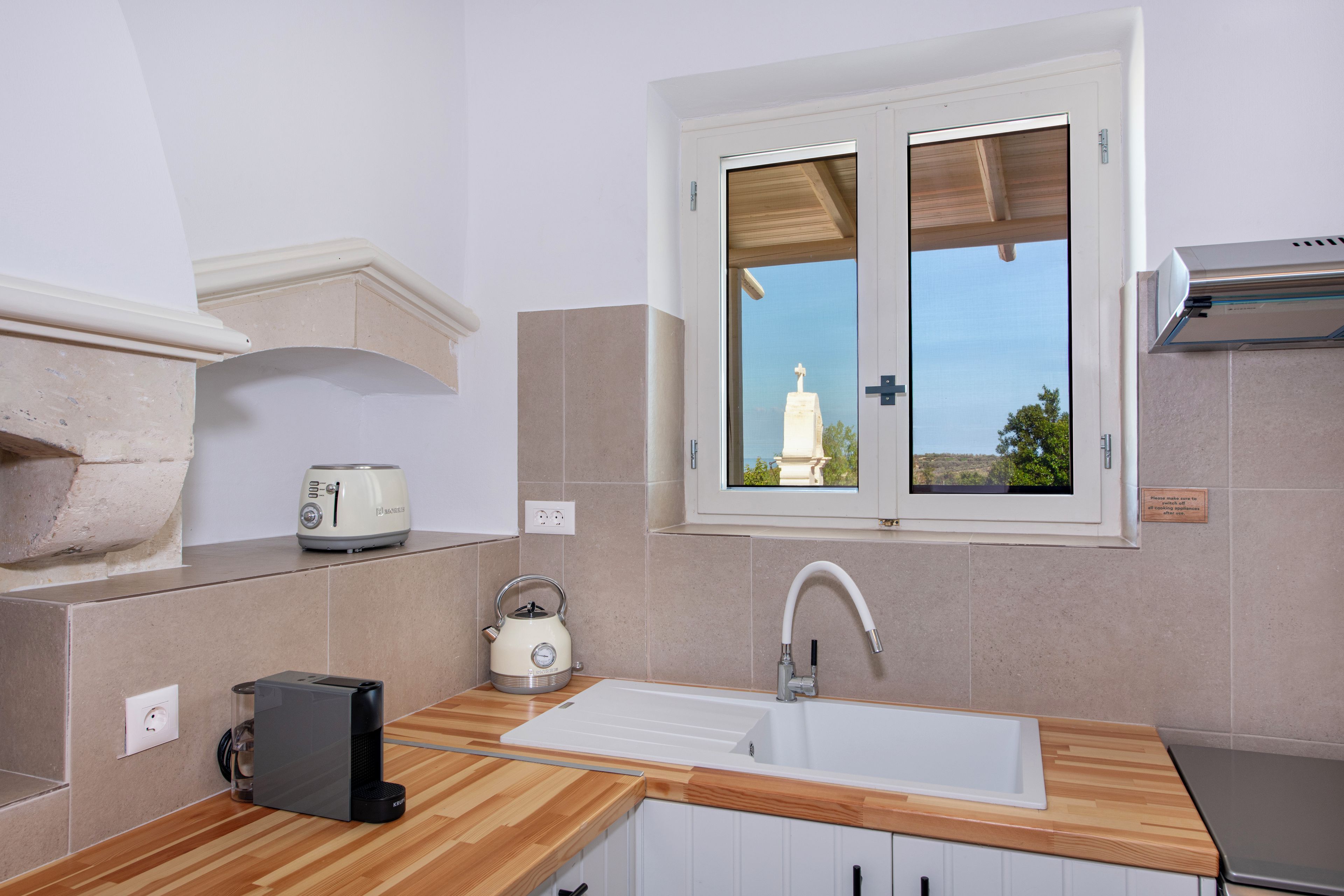 A kitchen with a window, a toaster, a kettle, and a sink.