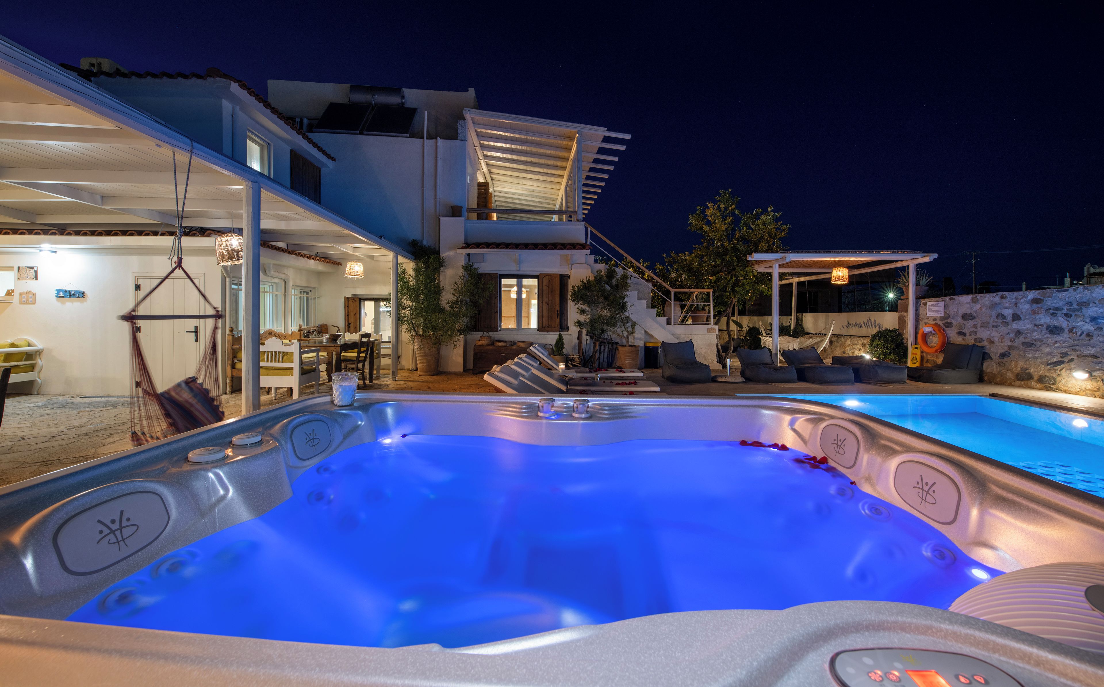 A modern outdoor hot tub area with a pool, a covered seating area, and a staircase leading to an upper level.