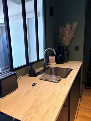 A kitchen with a marble countertop, a stainless steel sink, a toaster, a vase with dried plants, and a window with blinds. - Aix-en-Provence, Air-Conditioned Apartment with a Terrace (Aix-en-Provence)