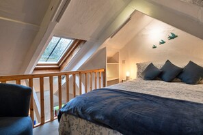 A bedroom with a sloped ceiling, a bed with a patterned bedspread, a nightstand, and a window with a view of trees. - Cottage Near Beaches Cornwall (Wadebridge)