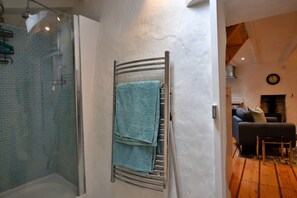 A bathroom with a glass shower enclosure, a towel rack with a folded towel, and a visible clock on the wall. - Cottage Near Beaches Cornwall (Wadebridge)