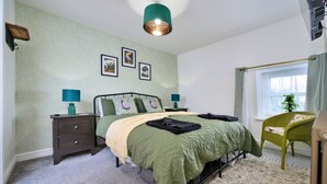 A bedroom with a bed, nightstands, a chair, a window with curtains, and wall-mounted pictures. - Scenic Snowdonia Border Cottage for 4 (Caernarfon)