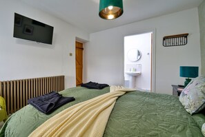 A bedroom with a bed, a television, a radiator, a door, a mirror, a sink, and a nightstand. - Scenic Snowdonia Border Cottage for 4 (Caernarfon)
