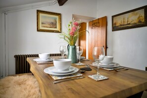 Ein Esstisch ist mit weißen Tellern, Schüsseln und Besteck gedeckt, dazu stehen eine Blumenvase und eine grüne Karaffe.