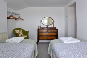 Une chambre avec deux lits, une commode, un miroir, une chaise et un radiateur.