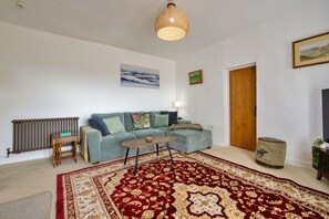 A living room with a sofa, a coffee table, a patterned rug, a radiator, and a door. - Scenic Snowdonia Border Cottage for 4 (Caernarfon)