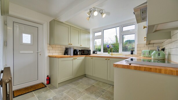 A kitchen with white cabinets, a microwave, a kettle, and a window with a view of greenery. - Scenic Snowdonia Border Cottage for 4 (Caernarfon)