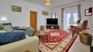 A living room with a sofa, a chair, a television, a rug, and a window with curtains. - Scenic Snowdonia Border Cottage for 4 (Caernarfon)