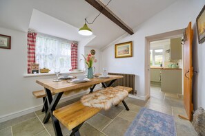 Un coin repas avec une table en bois, des bancs, un plaid en fourrure et une fenêtre avec des rideaux.