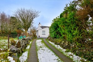 A narrow, snow-covered path leading to a white house with a chimney, surrounded by greenery and a stone wall. - Scenic Snowdonia Border Cottage for 4 (Caernarfon)