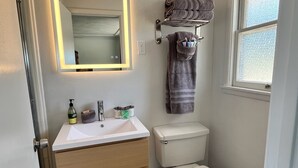 A bathroom with a white sink, a toilet, a towel rack, and a mirror with a light.