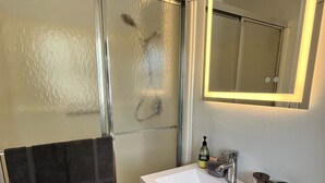 A bathroom with a glass shower door, a white sink, and a mirror above it.