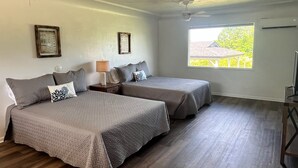 A room with two beds, a ceiling fan, a window with a view, and a framed picture on the wall.