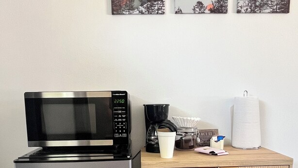 Eine Küchenzeile mit einem Edelstahlkühlschrank, einer Mikrowelle, einer Kaffeemaschine und einem Holzkasten.
