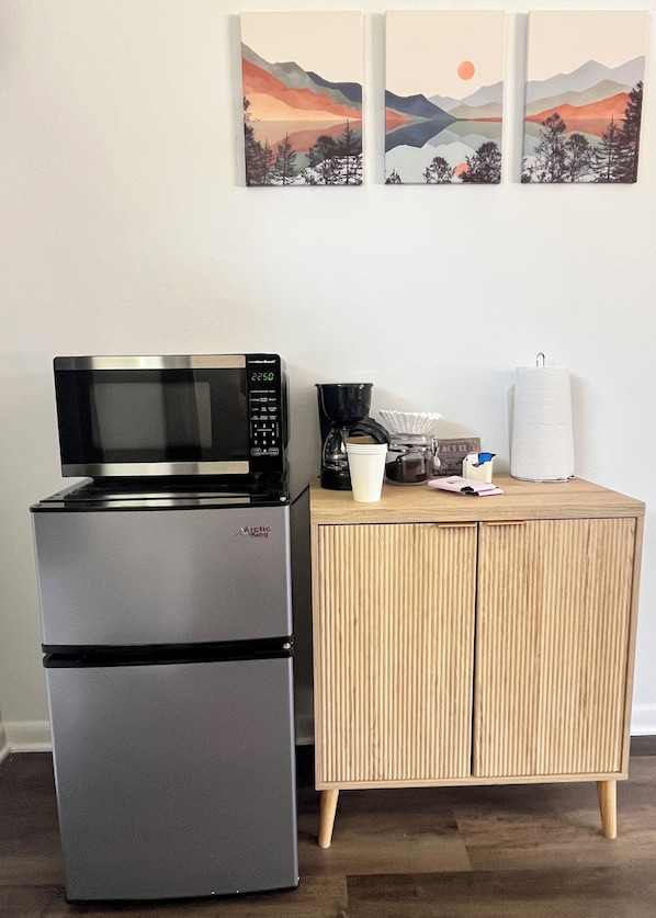 A kitchen area with a stainless steel refrigerator, a microwave, a coffee maker, and a wooden cabinet.
