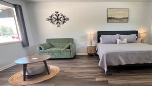 Ein Schlafzimmer mit einem Bett, einem grünen Sessel, einem kleinen Tisch, einer Wandleuchte und einem Gemälde.