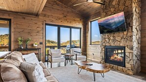 Un salon chaleureux avec une cheminée en pierre, des murs en bois et de grandes fenêtres donnant sur un paysage magnifique.
