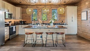 Une cuisine moderne avec des murs en bois, un îlot central doté de tabourets, des appareils en acier inoxydable et des luminaires suspendus.
