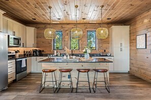 Eine moderne Küche mit Holzwänden, einer zentralen Kochinsel mit Hockern, Edelstahlgeräten und Pendelleuchten.