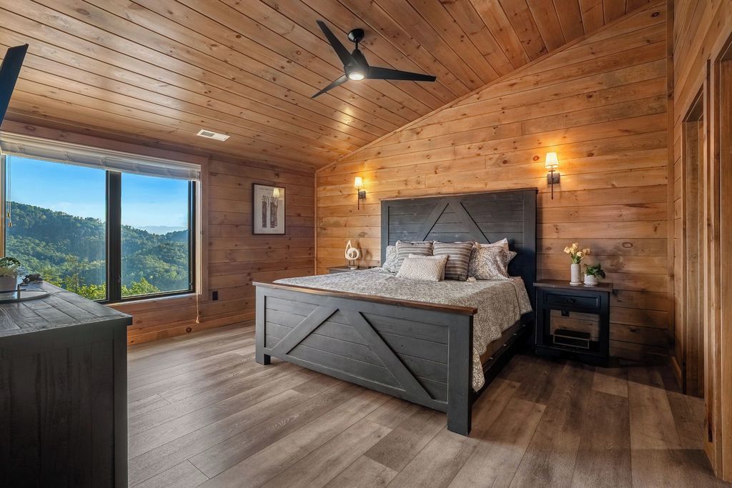 A bedroom with a bed, wooden ceiling, and a large window.