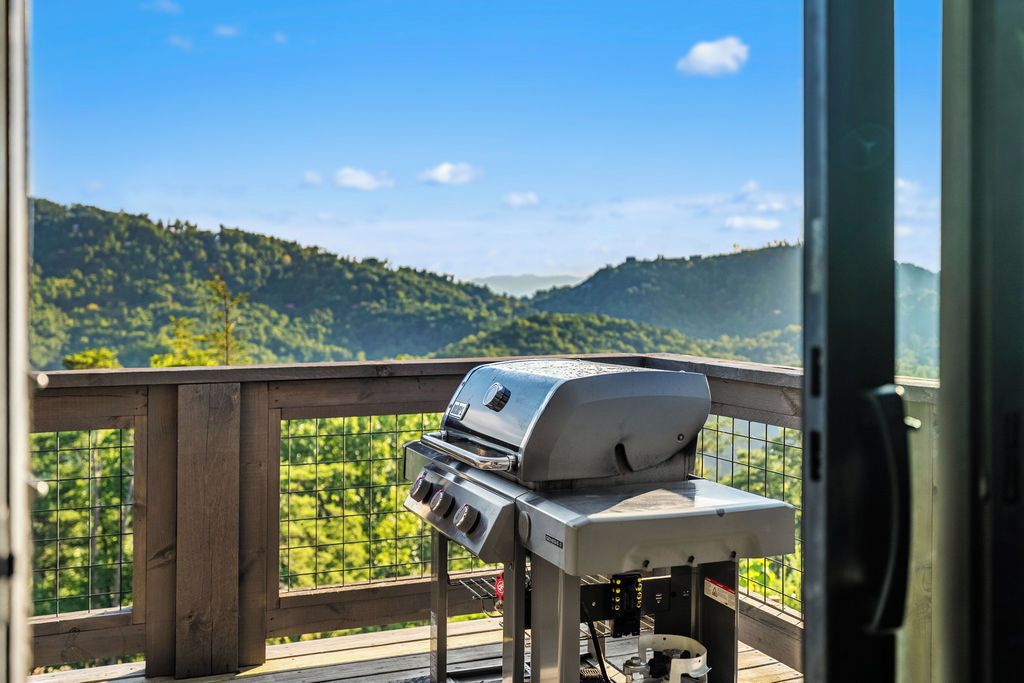 A grill on a balcony with a view of a forested hillside.