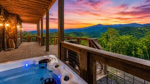 Un bain à remous sur une terrasse en bois, avec vue sur les montagnes et un coucher de soleil.