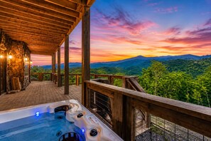 Ein Whirlpool auf einer Holzterrasse mit Blick auf Berge und einen Sonnenuntergang.
