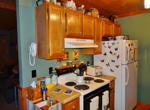 Une cuisine avec des meubles de rangement en bois, une cuisinière, un réfrigérateur et un téléphone fixé au mur.