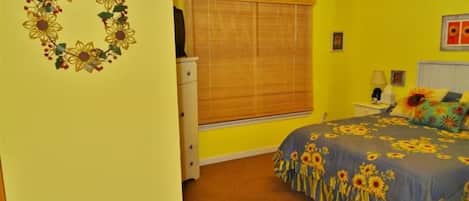 A bedroom with a bed, a dresser, a window with blinds, and a wall decoration.