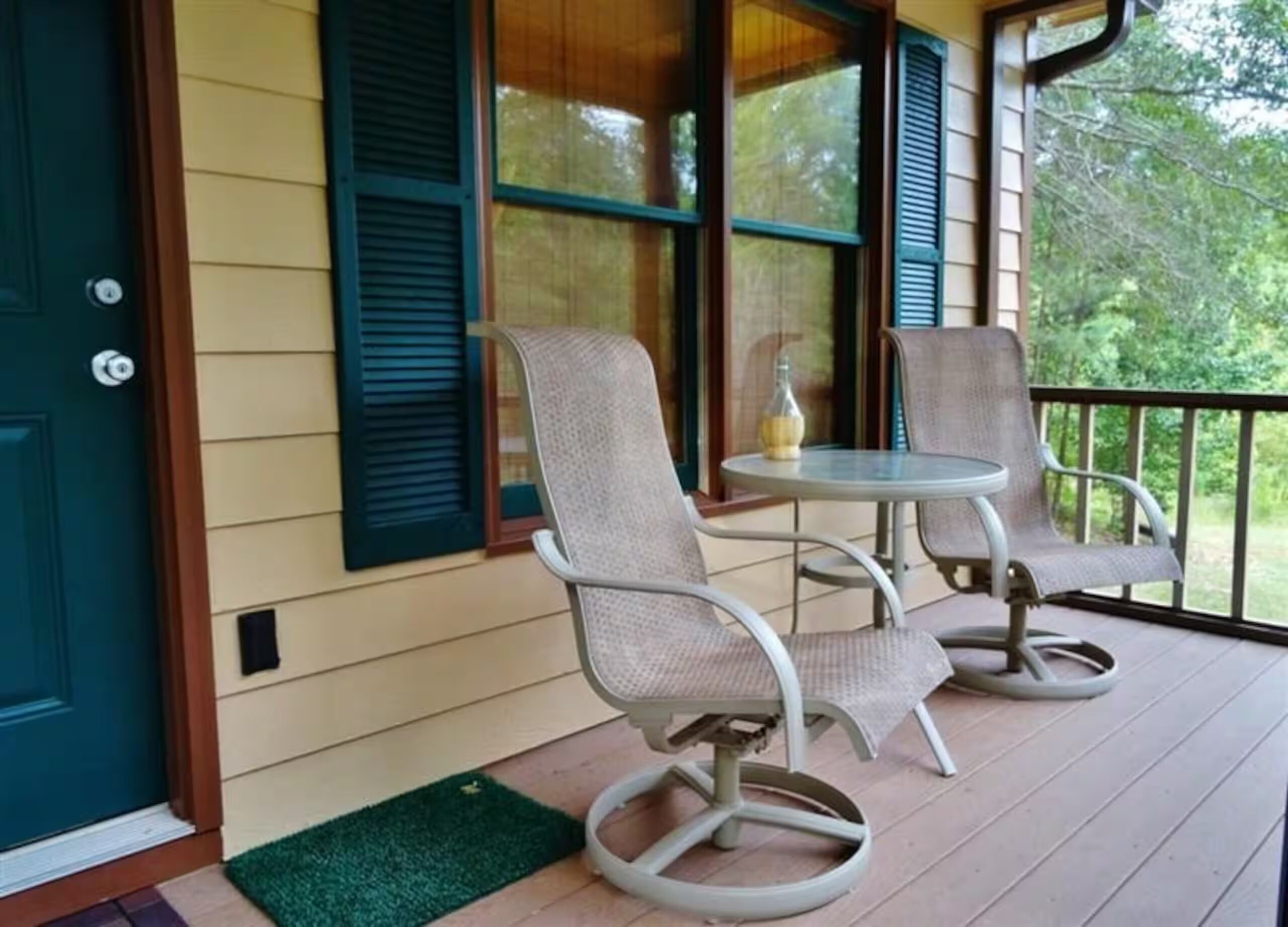 A porch with two chairs and a small table, a green doormat, and a door with a lock.
