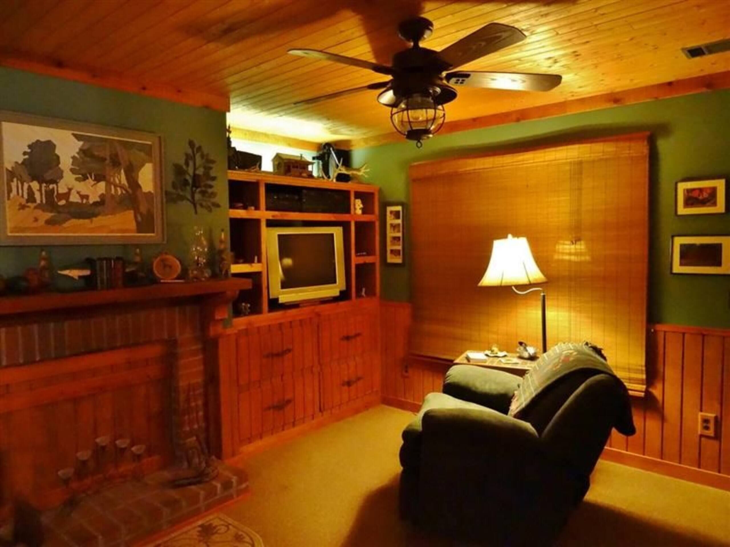 A cozy living room with a fireplace, a television, and a ceiling fan.