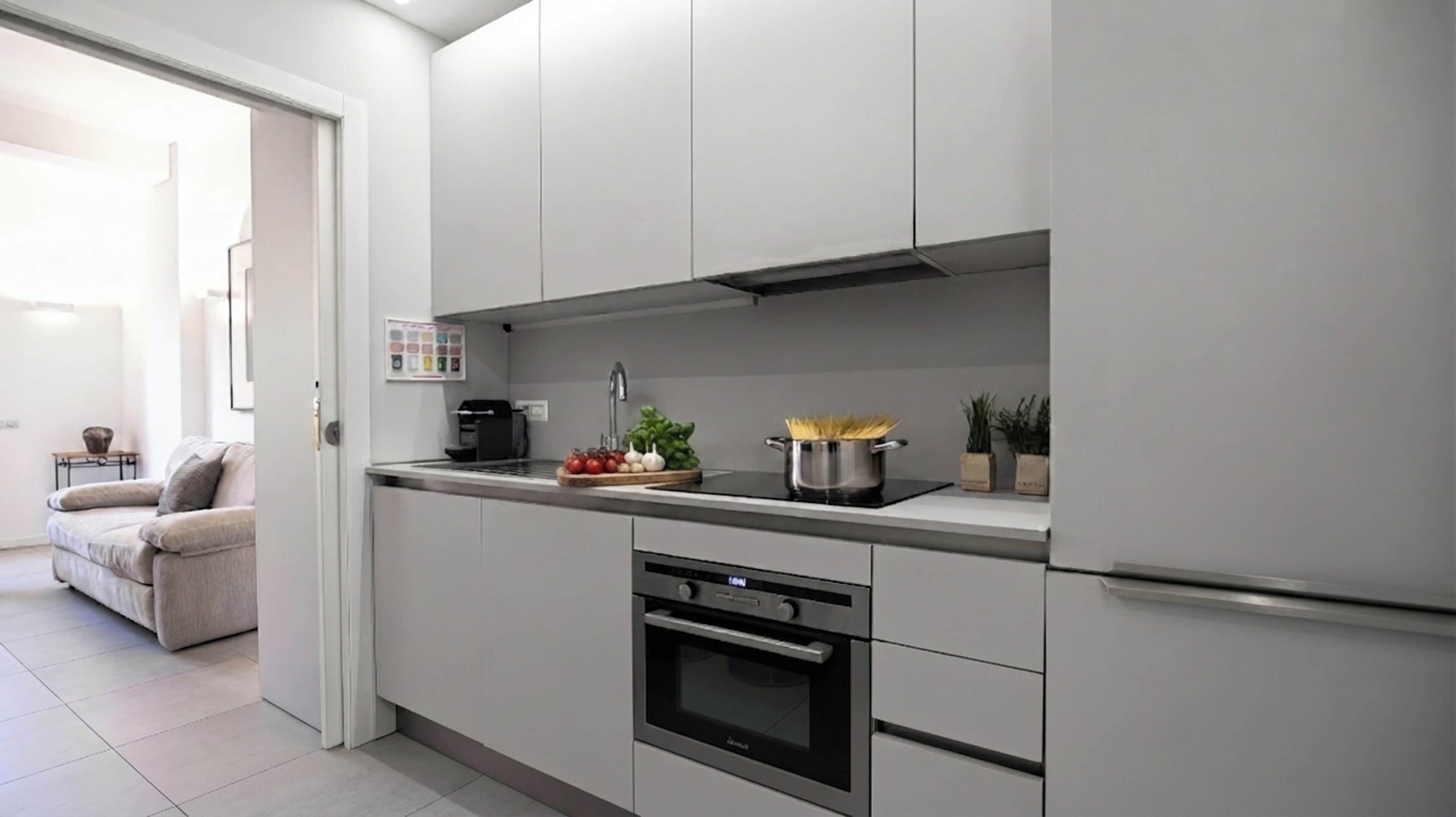 Een moderne keuken met witte kastjes, een inbouwoven en een roestvrijstalen afzuigkap.