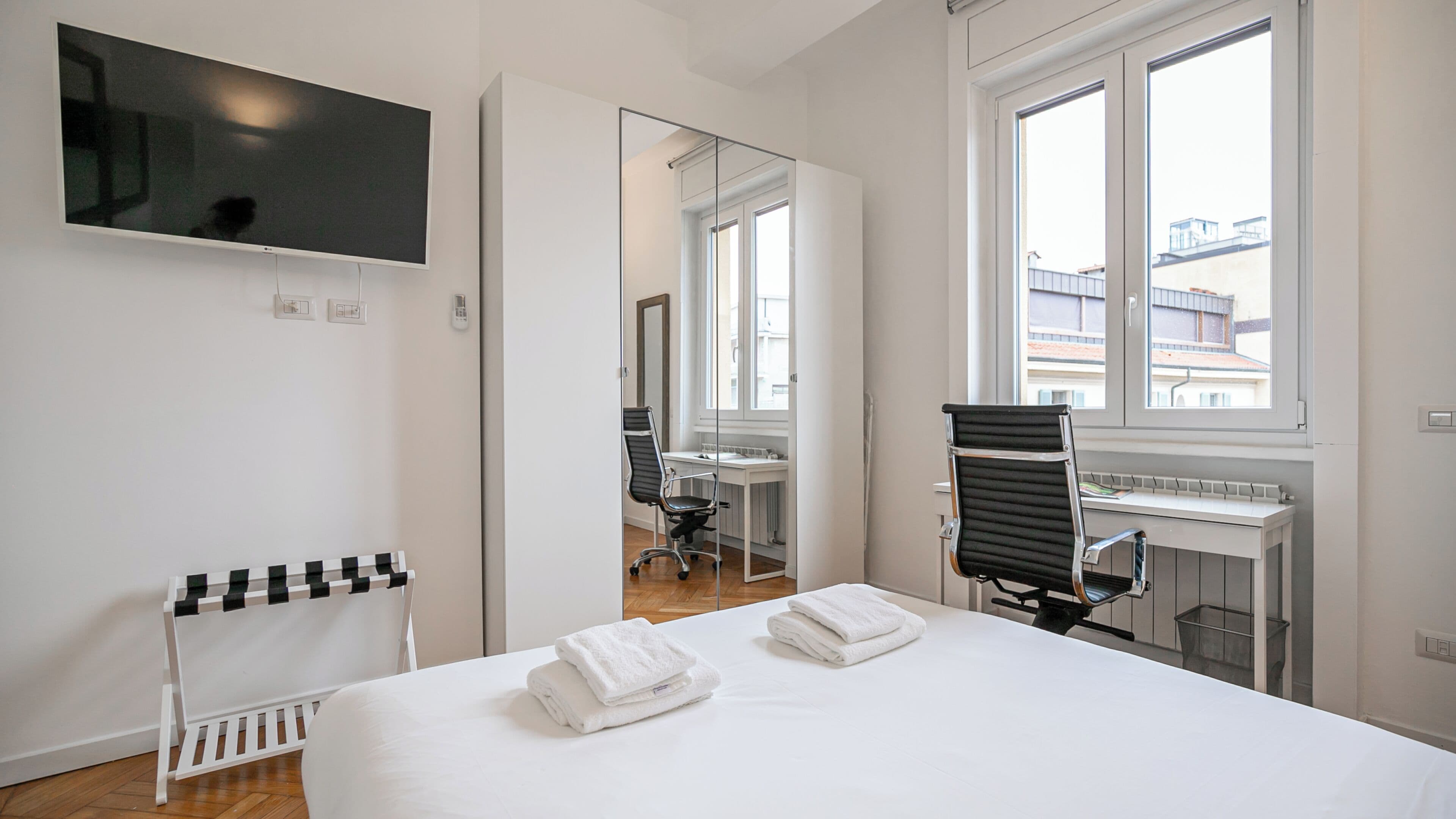 Une chambre d’hôtel avec un lit, un bureau, une chaise, une télévision et une fenêtre.