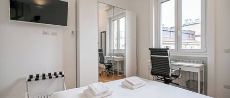 A hotel room with a bed, a desk, a chair, a TV, and a window.