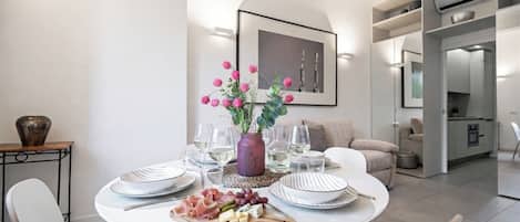 A modern dining area with a round table set for a meal, a vase with flowers, and a kitchen in the background.