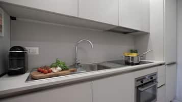 Een moderne keuken met een roestvrijstalen spoelbak, een koffieapparaat en een pan spaghetti op het aanrecht.